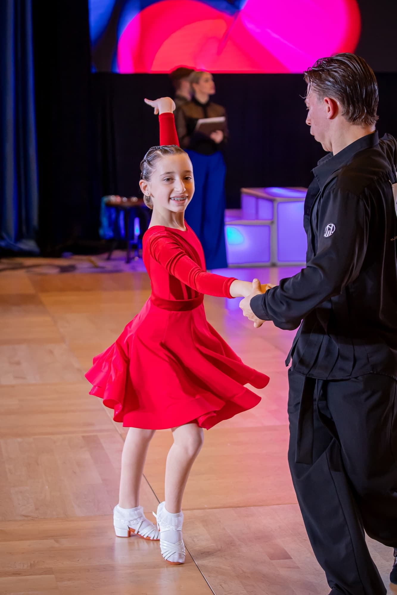 Junior Latin dancer in red, smiling mid-spin